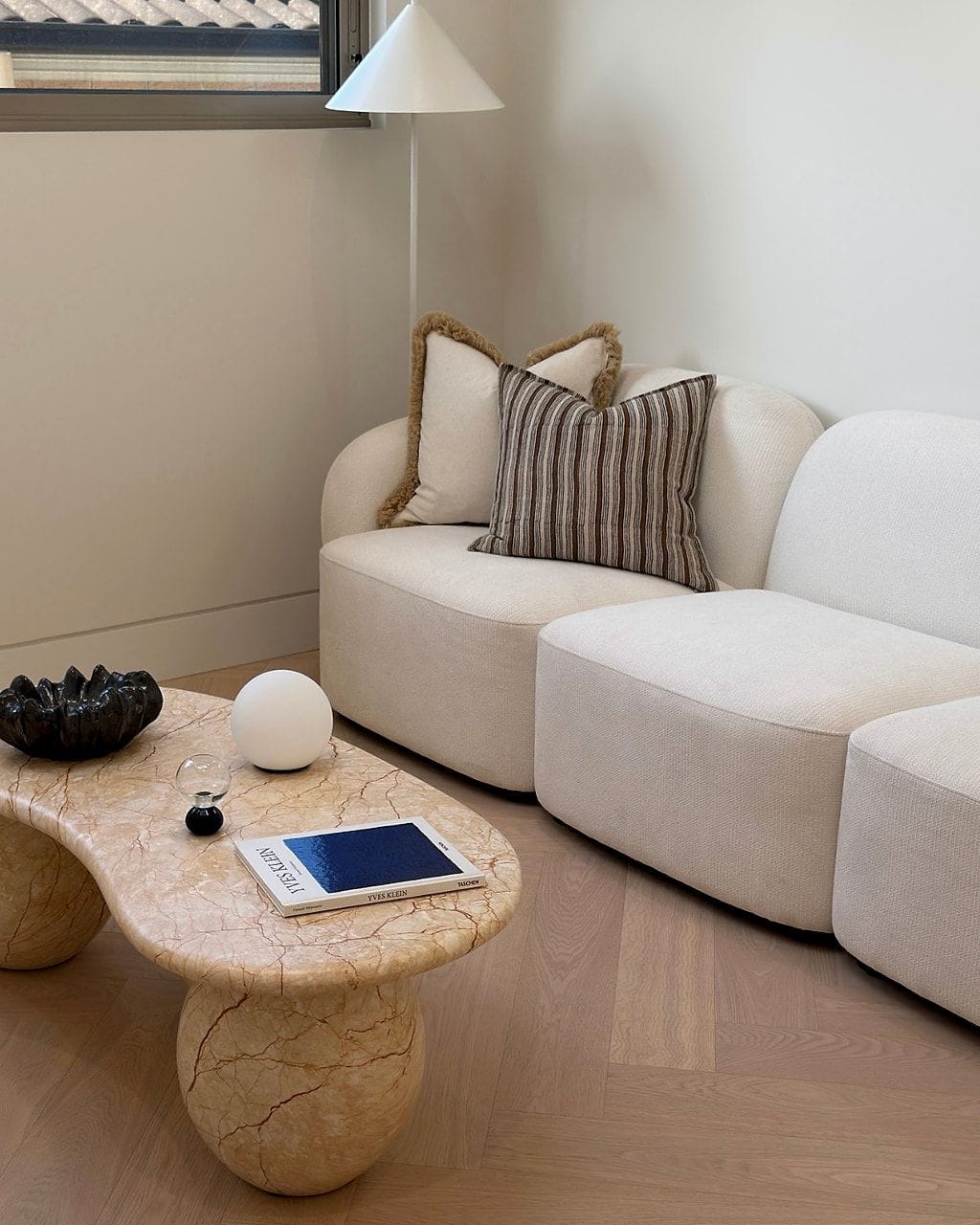Pale herringbone flooring in a living room with a curved white sofa and a stone coffee table