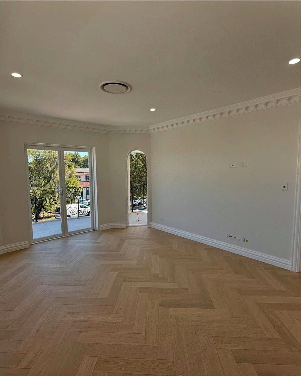 Herringbone oak flooring running the length of an empty room towards French doors