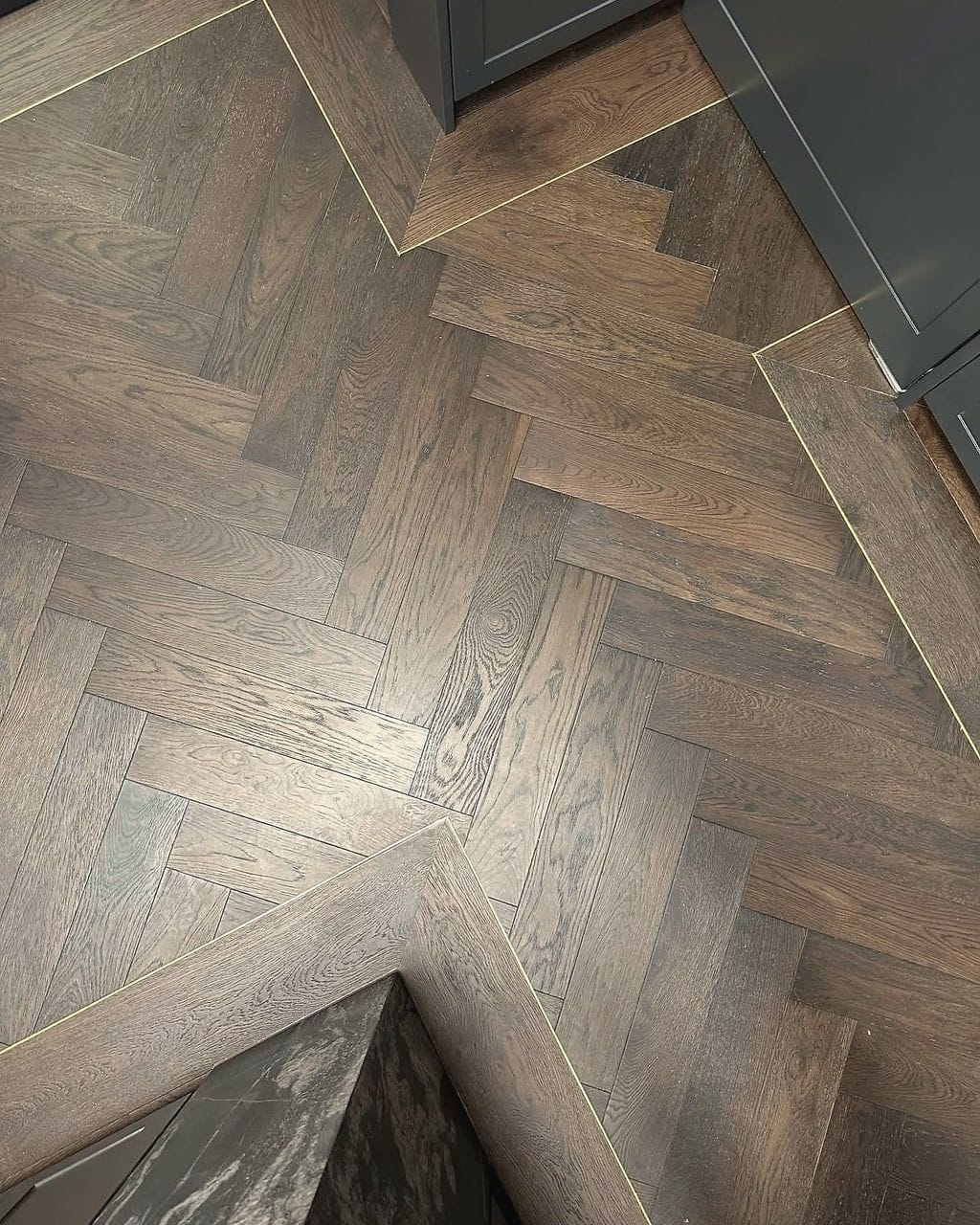 A slim brass inlay strip and a mitred border set into dark smoked oak herringbone