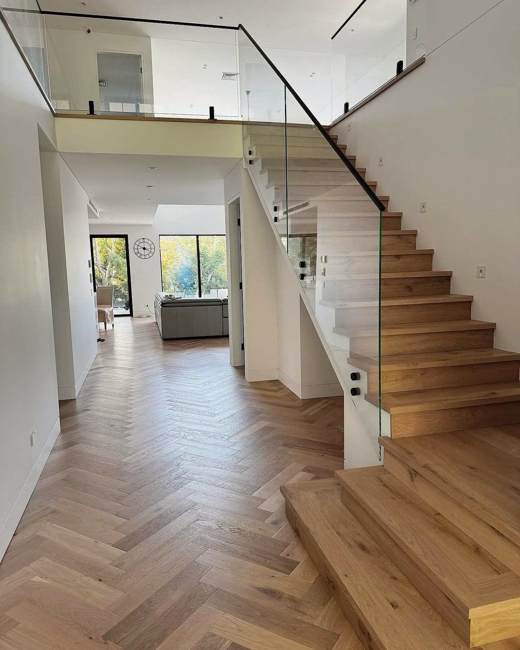 A herringbone hallway opening into a living area, timber stair treads and a glass balustrade alongside
